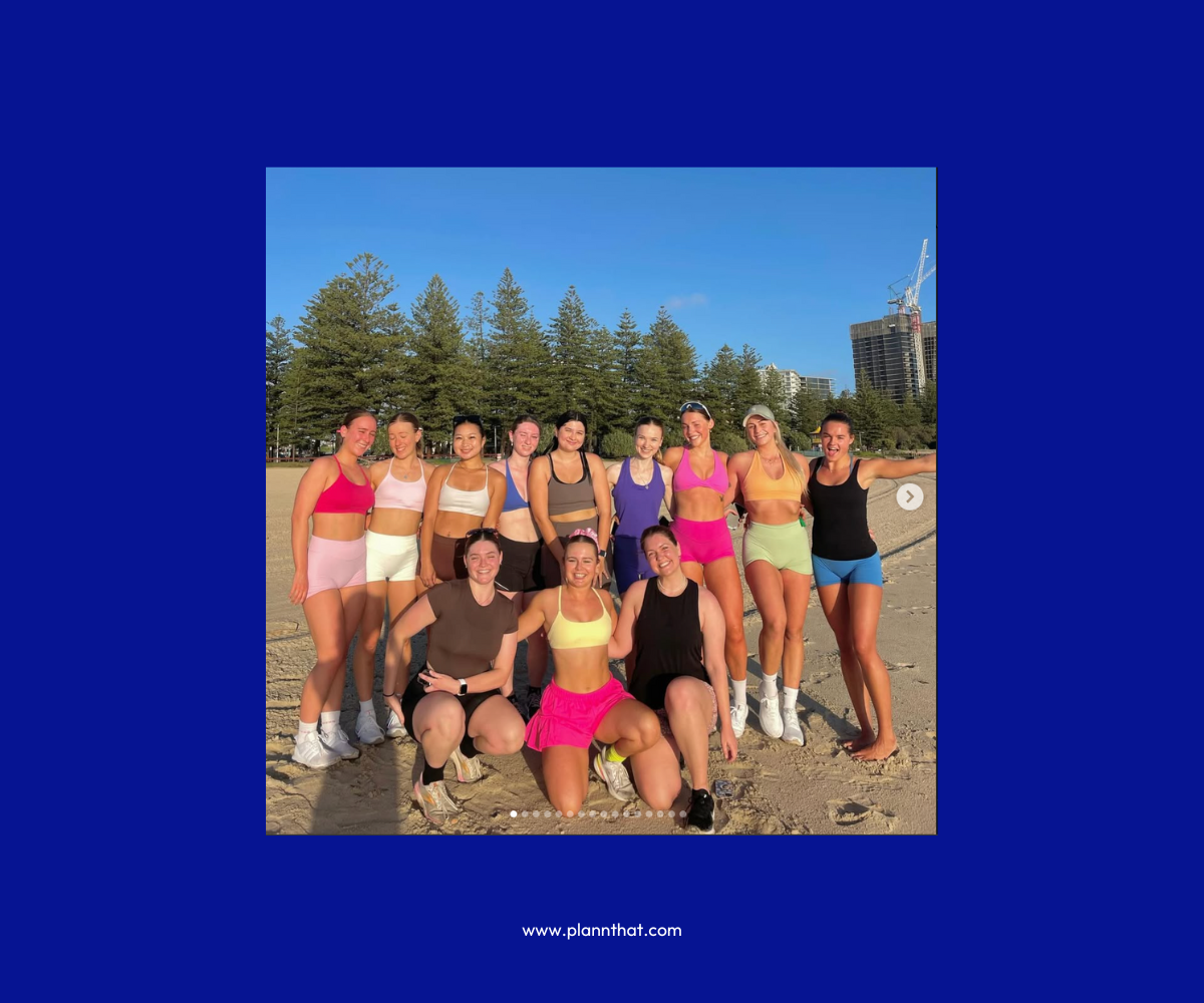 A group of young women pose on a beach in colorful athletic wear, smiling at the camera. 